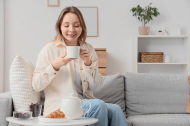 Oturma odasındaki kanepede çay içen genç bir kadın.