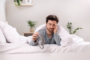 Uyku maskesi ve battaniyeli yorgun genç adam evde yatıyordu.