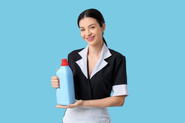 Mavi arka planda bir şişe deterjanı olan güzel bir oda hizmetçisi.