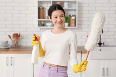 Genç bir kadın mutfakta toz bezi ve temizlik spreyi kullanıyor.