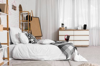 Yatak, raf ünitesi ve çekmeceleri olan bir gencin odası.