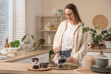 Mutfaktaki masada çaydanlık ve kuru çayla genç bir kadın.