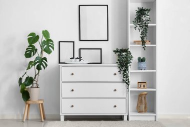 Raflama ünitesi, çekmece sandığı ve odadaki beyaz duvarda boş fotoğraf çerçeveleri.