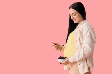 Pembe arka planda kuru eriği olan genç hamile bir kadın.