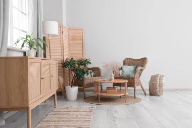 Oturma odasındaki beyaz duvarın yanında hasır koltuklar, masa ve katlanır ekran.