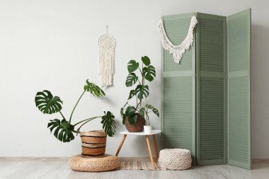 Katlanan ekran, masa ve Monstera çiçekleri beyaz duvarın yanında.