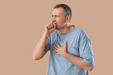 Bej arka planda öksüren olgun bir adam.