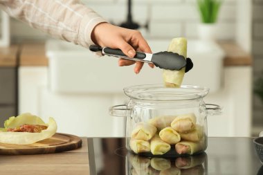 Kadın mutfaktaki fırında pişirme kabından lahana sarması alıyor, yakın plan.