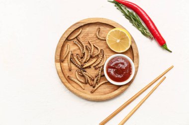 Kızarmış kurtlu ahşap tabak, limon, kırmızı biber ve beyaz arka planda bir kase ketçap.