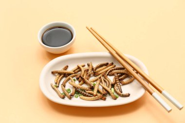 Kızarmış kurtlu tabak ve turuncu arka planda soya sosu.