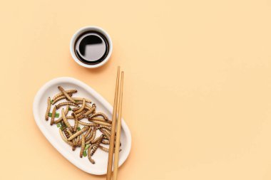 Kızarmış kurtlu tabak ve turuncu arka planda soya sosu.