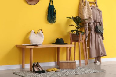 Bank, ev bitkisi, merdiven, ceket ve çantalar koridordaki sarı duvarın yanında.