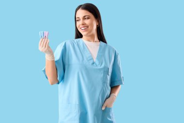 Mavi arka planda diş modelleri olan kadın dişçi.