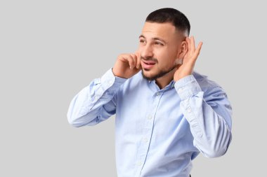 Genç işadamı gri arka planda bir şeyler duymaya çalışıyor.