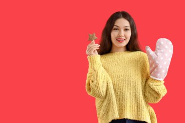 Yıldız şeklinde kurabiyesi ve kırmızı arka planda fırın eldiveni olan genç Asyalı kadın.