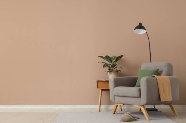 Koltuk, terlik ve ev bitkisi kahverengi duvarın yanındaki komodinin üzerinde.