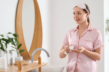 Genç bir kadın banyoda kozmetik ürünler kullanıyor.