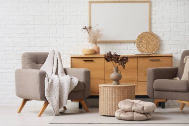 Koltuklar, kahve masası ve beyaz tuğla duvarın yanındaki çekmeceler.