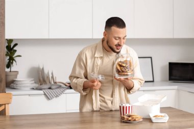 Mutfakta açık kurabiye kavanozu olan genç adam.