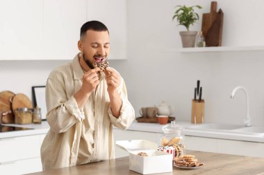 Genç adam mutfakta kurabiye yiyor.