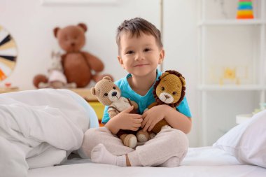 Evde yatağında oyuncakları olan sevimli bir çocuk.