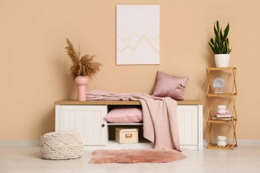 Oturma odasındaki bej duvarın yanında raflı ve farklı mercan dekorlu bir elbise.