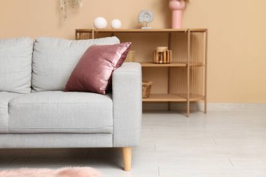 Oturma odasındaki bej duvarın yanında mercan yastıklı ve şifoniyerli kanepe.