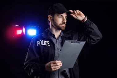 Siyah arka planda yanıp sönen siren ışıklarına karşı elinde dosya olan erkek polis memuru.