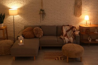 Beyaz tuğla duvarın yanında puf, kanepe ve parlayan lambalar olan karanlık oturma odasının içinde.