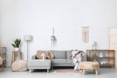 Beyaz tuğla duvarın yanında pufları ve kanepesi olan aydınlık oturma odasının içinde.