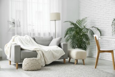 Aydınlık oturma odasının içinde kanepe, yer lambası ve pencerenin yanında puf var.