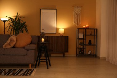 Kanepesi ve bej duvarın yanında parlayan lambaları olan karanlık oturma odasının içinde.