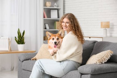 Genç bayan kanepede oturuyor ve sevimli Corgi köpeğine sarılıyor.