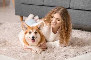 Evde yerde yatan sevimli Corgi köpeği olan genç bir kadın.