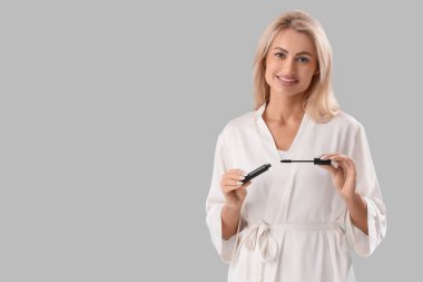 Gri arka planda maskara süren bornozlu güzel bir kadın.