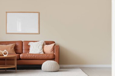 Oturma odasının içinde kahverengi kanepe, puf ve boş çerçeve.