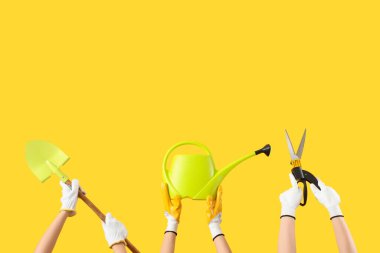 Sarı arka planda bahçe aletleri olan kadın elleri