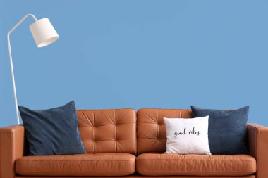 Mavi arka planda yastıkları ve lambası olan rahat bir kanepe.