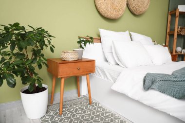 Yatağın yanında çiçek ve hasır sepet olan bir komodin.