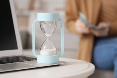 Evde para sayan kadınlara karşı dizüstü bilgisayarlı kum saati, yakın plan.