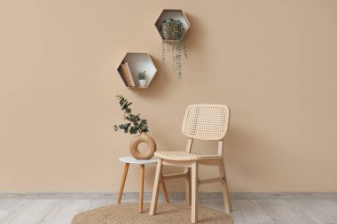 Kahve masalı rahat ahşap sandalye, okaliptüs dalları vazosu ve bej duvarın yanındaki ev bitkileri.