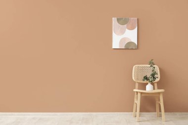 İçinde okaliptüs dalları ve kahverengi duvarda asılı bir resim olan rahat ahşap sandalye.