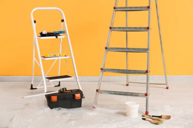 Aletleri olan bakım merdivenleri ve sarı duvarın yanındaki boya aletleri.