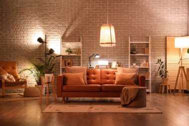 Modern oturma odasının içinde kahverengi kanepe, koltuk, işyeri, raf üniteleri ve akşamları parlayan lambalar