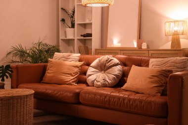 Akşamları kahverengi kanepe, hasır sepet ve parlayan lambayla modern oturma odasının içinde.