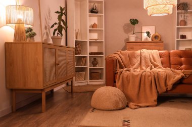 Modern oturma odasının içinde kahverengi kanepe, çekmeceler, raf ünitesi ve akşam lambaları.