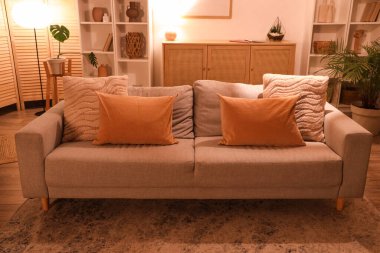 Gri koltuklu modern oturma odasının içi, çekmeceler, raf üniteleri ve akşamları parlayan lambalar.