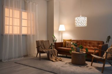 Oturma odasının içinde kahverengi kanepe, koltuklar ve gece lambaları var.