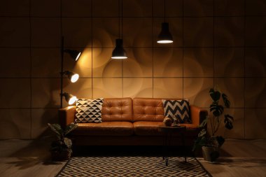 Kahverengi kanepesi, masası ve parlak lambaları olan karanlık oturma odasının içinde.