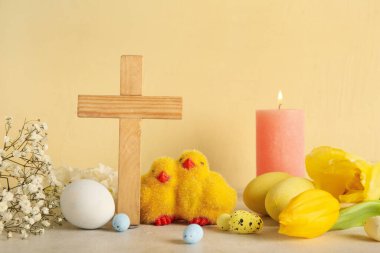 Piliçlerle ahşap haç, beyaz masaya boyanmış yumurta ve çiçekler, sarı grunge arka plana karşı. Paskalya kutlaması